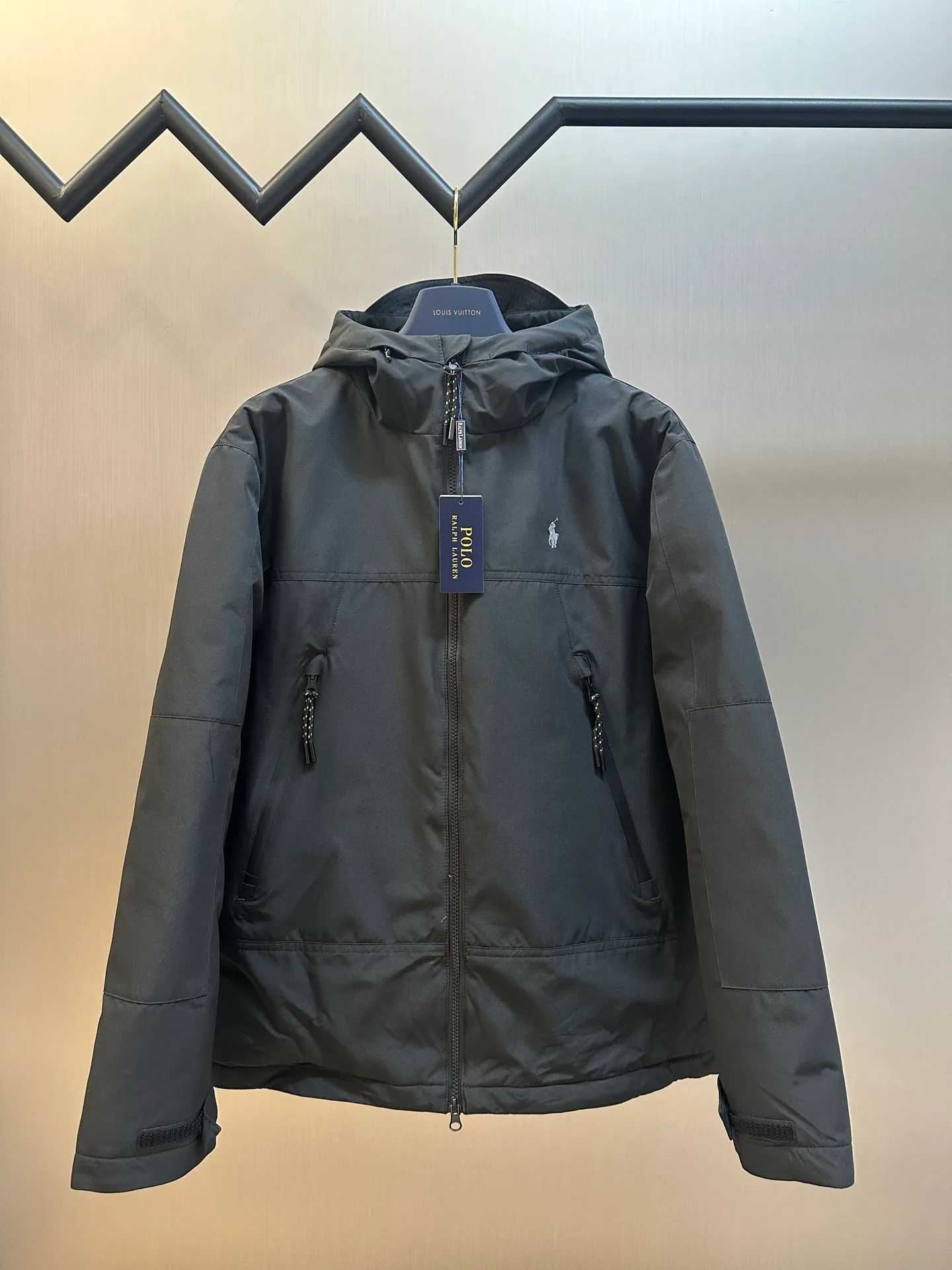 P970 Ralph Lauren logo hooded down jacket. The density of high-density nylon taffeta is about 210T-300T. The surface is smooth and slightly matte. It has excellent windproof and waterproof performance (with DWR water-repellent treatment). It has strong wrinkle resistance and is easy to care for. It is in line with the positioning of American casual "durable and practical".  The inner lining is made of 100% polyamide. The high-density and tight weaving process prevents fine lint from getting out of the gaps in the fabric. The smooth surface improves the putting on and taking off experience, and the excellent wear and tear resistance ensures damage caused by frequent use, while the light and soft texture does not affect the overall weight.  It uses 90 white duck down with a weight of 220g to ensure excellent thermal insulation performance. After strict screening and processing, the velvet is not easily drilled, ensuring durability. The classic jacket has a slightly loose fit, with slightly dropped shoulder lines (the shoulder width is 1-2cm wider than the standard fit). The length reaches the hips, and the sleeves are slightly tapered straight sleeves, taking into account freedom of movement and casual style.  The adjustable Velcro on the cuffs allows you to freely adjust the tightness according to the thickness of your wrist and personal preferences, effectively preventing cold wind from intruding, and improving the warmth performance. Two zippered pockets on the front are convenient for placing frequently used items, and the zipper design ensures that items are not easily lost. A built-in pocket on the left side of the chest provides a safe storage space for some small private items.  The drawstring design at the hem allows you to adjust the shape of the jacket according to your body shape and dressing needs. Whether it is loose and casual or slim and neat, you can easily control it.  Polo horse logo on the left chest: flat satin stitch embroidery (satin embroidery), using 100% polyester high color fastness embroidery thread (the color number is consistent with the brand's standard red color card), the stitch density is 12-15 stitches/cm, the outline of the horse logo is clear, and the details of the rider and horse are burr-free. Precise positioning through the template (12cm from the bottom of the collar and 8cm from the placket) ensures symmetry and centering.  size：s m l xl